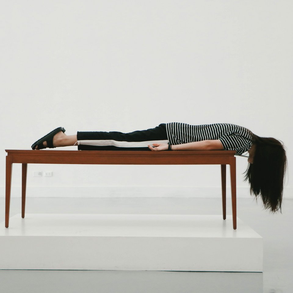 Schmuckbild: Ein Mädchen liegt auf dem Bauch auf einem Tisch - Ihre langen Haare hängen über den Rand